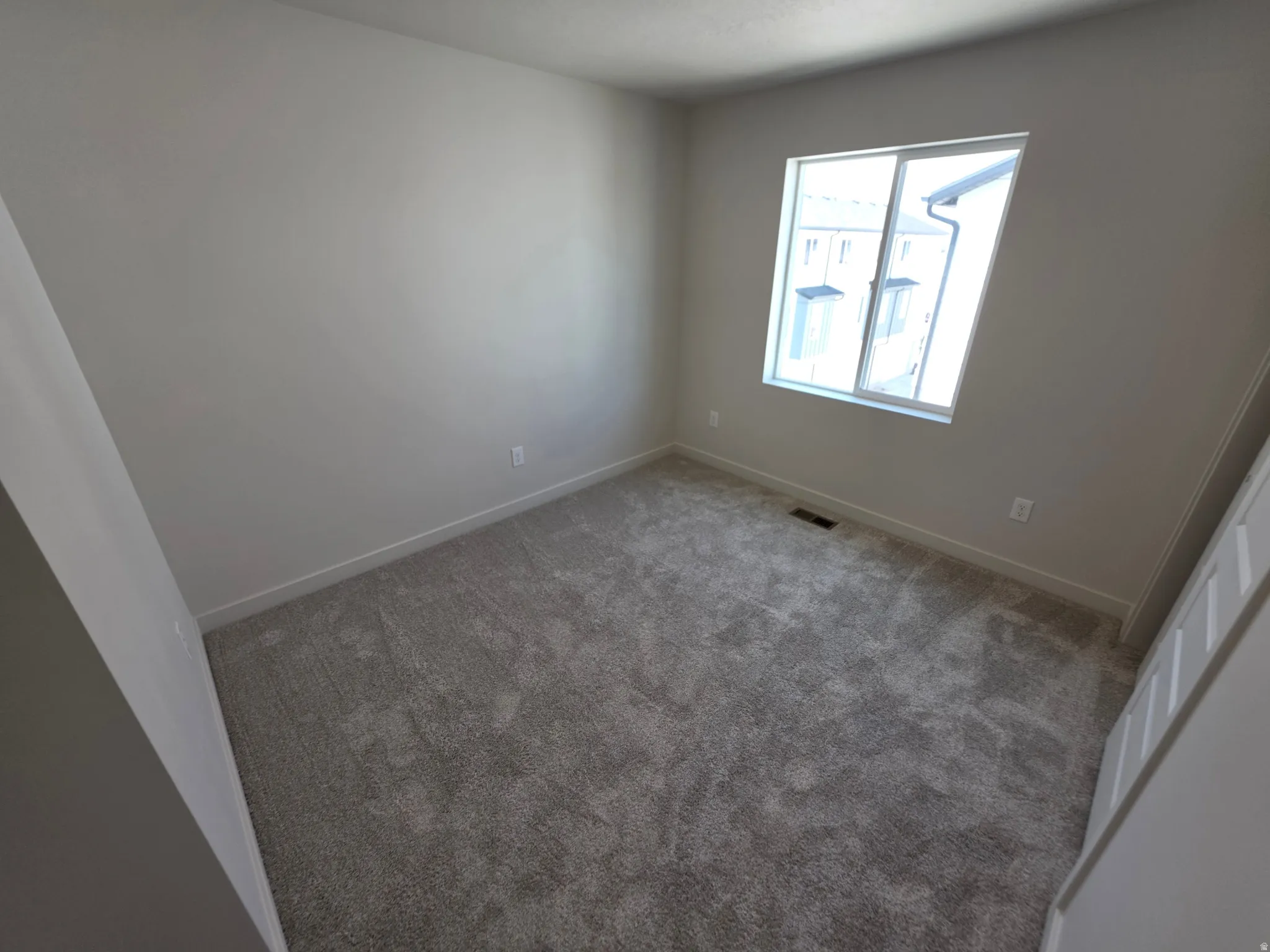 Neutral wall colors with a single window, grey carpeting, and white trim