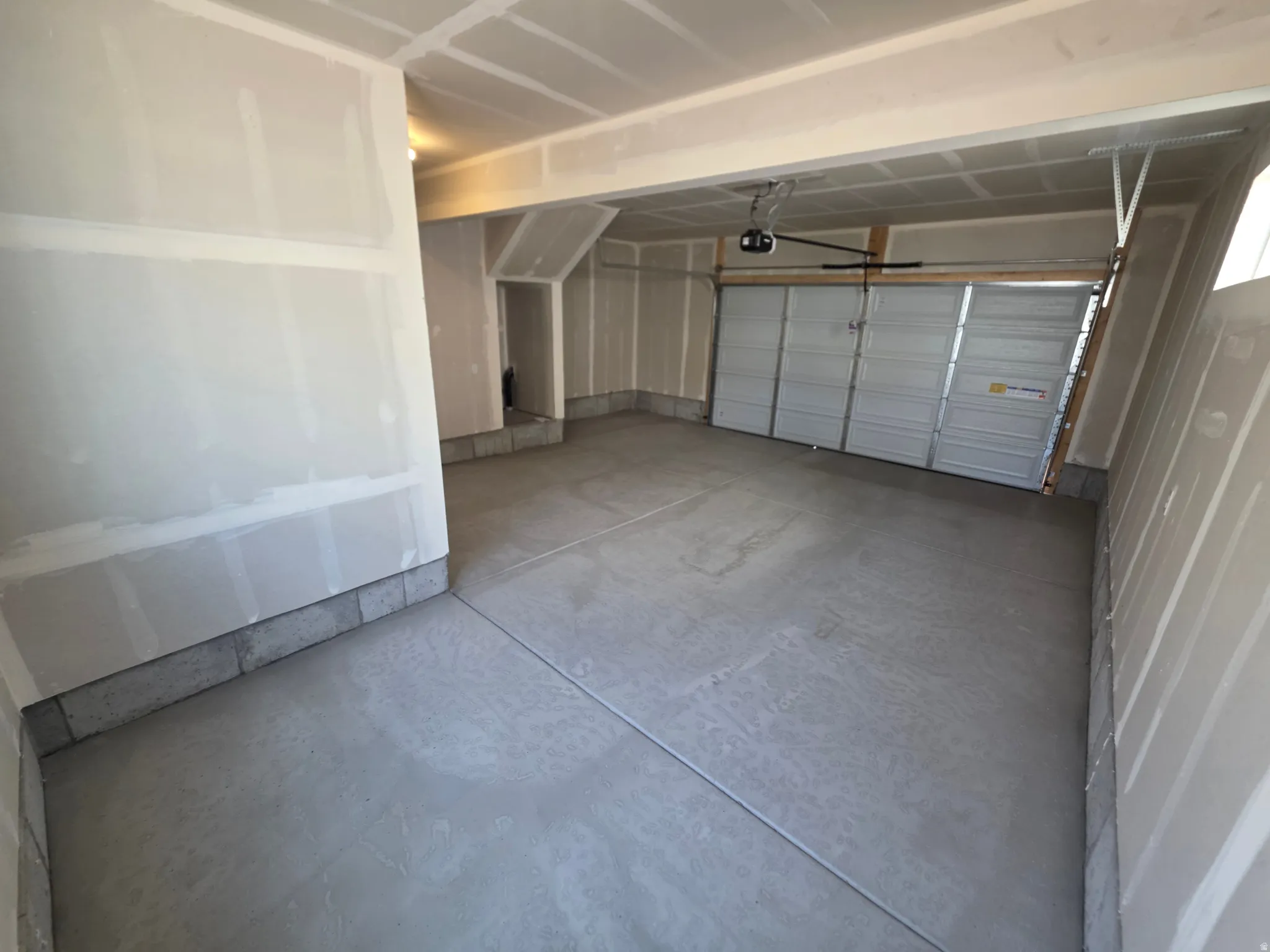 Spacious garage featuring a concrete floor, automatic garage door opener, and unfinished drywall walls
