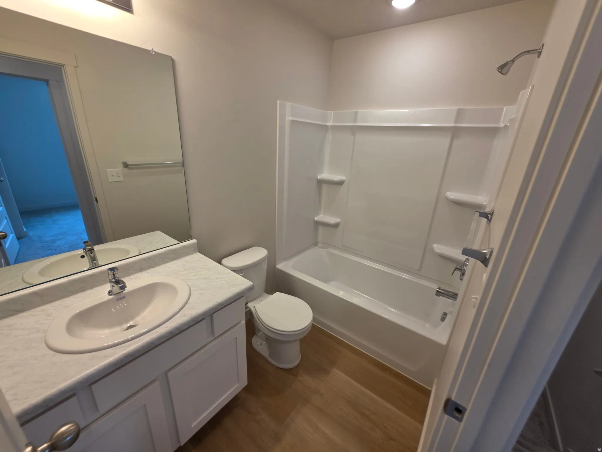 Bathroom featuring a white vanity with an integrated sink, a large wall-mounted mirror, a toilet, a white shower/tub combination, and wood-finish flooring