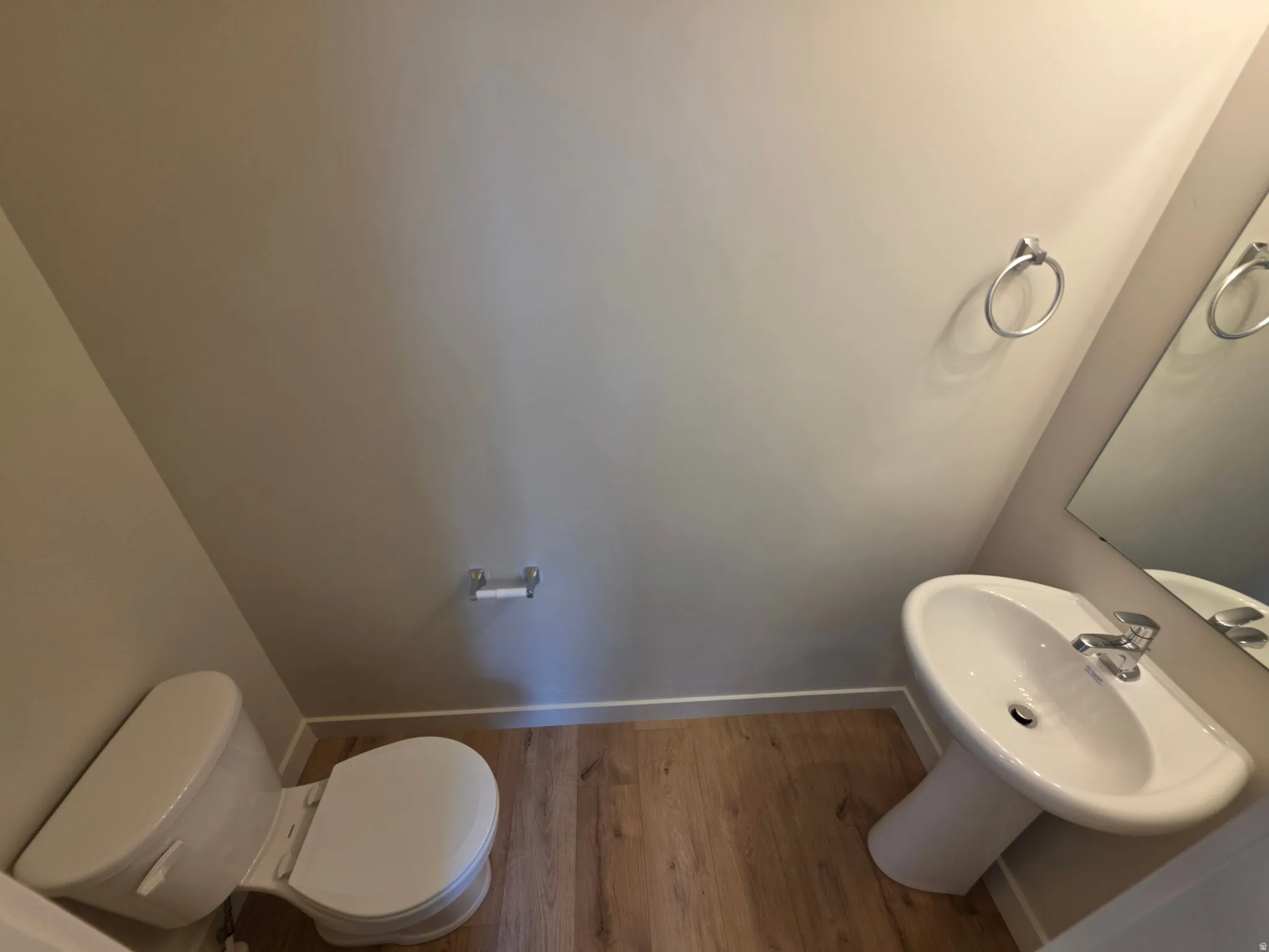 Pedestal sink with chrome faucet, wood-finish flooring, and wall-mounted mirror