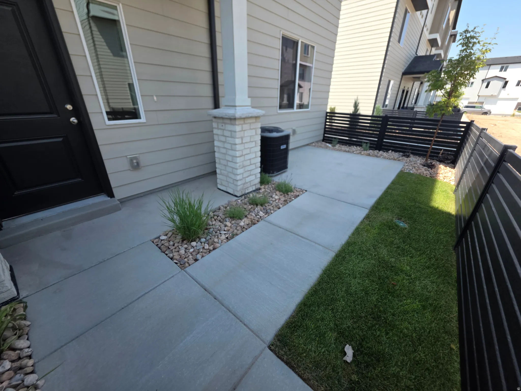 Concrete walkway with integrated rock beds and plantings, leading to a modern black entry door