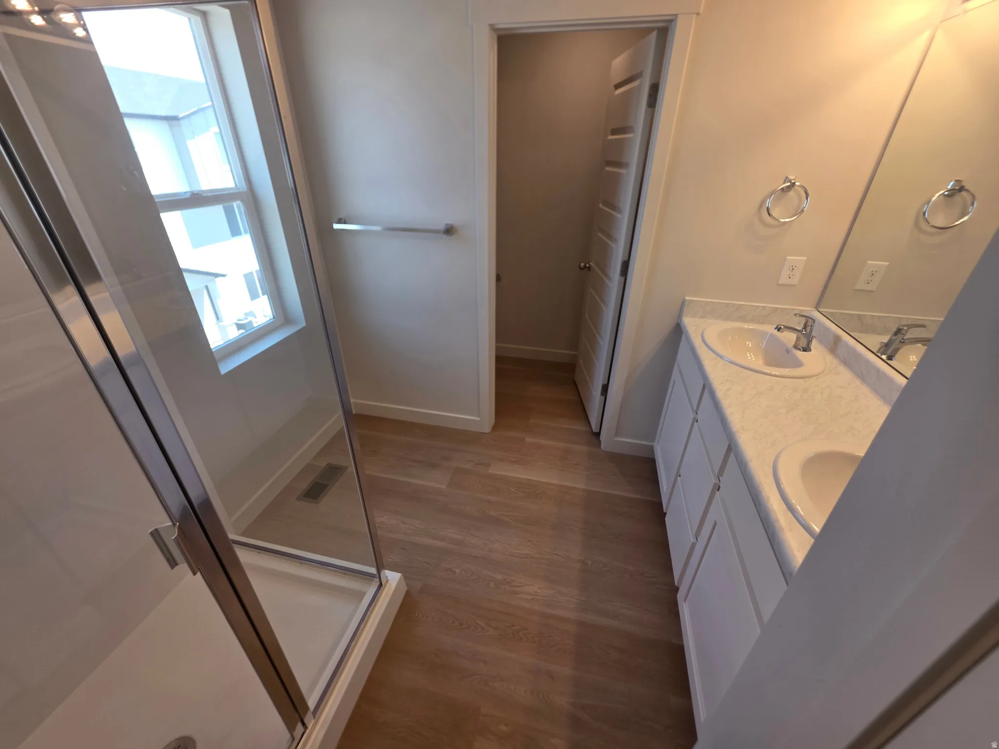 Dual vanity with undermount sinks, wood-finish flooring, glass-enclosed shower, transom window, and paneled door