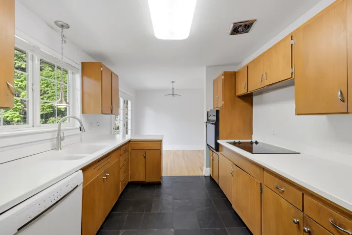 Galley kitchen featuring light wood-finish cabinetry, solid surface countertops, a dual basin sink with a pull-down faucet, and a four-burner electric cooktop