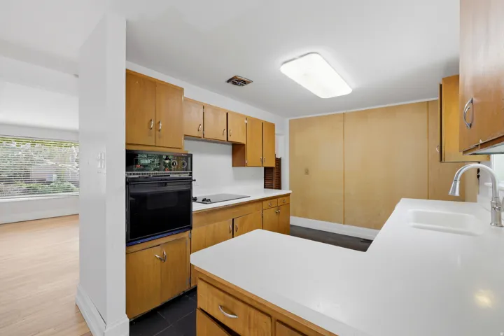 Wood-finish cabinetry paired with white countertops and a stainless steel faucet