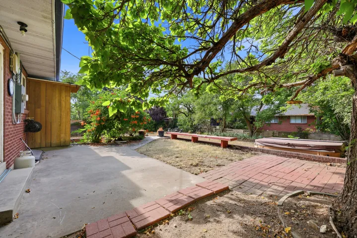 Brick patio with concrete walkway, a wooden storage shed, and mature trees