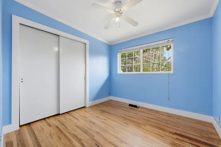 Hardwood flooring, white crown molding, ceiling fan, sliding closet doors, and a window with white trim