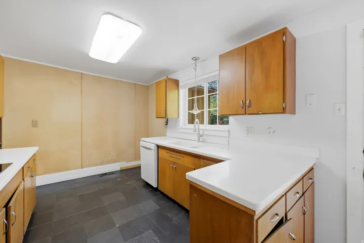 Hardwood cabinetry, white countertops, stainless steel sink, tile flooring, and a large window