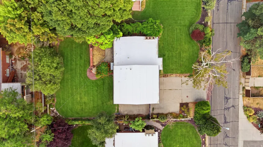 Expansive lot featuring a white roof, mature trees, manicured lawns, paved driveway, and brick hardscaping