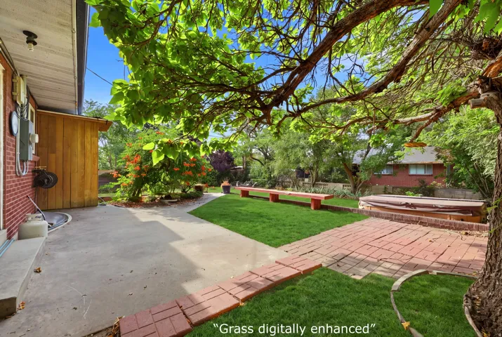 Expansive rear yard featuring a concrete patio, brick paver accents, a built-in spa, and mature landscaping