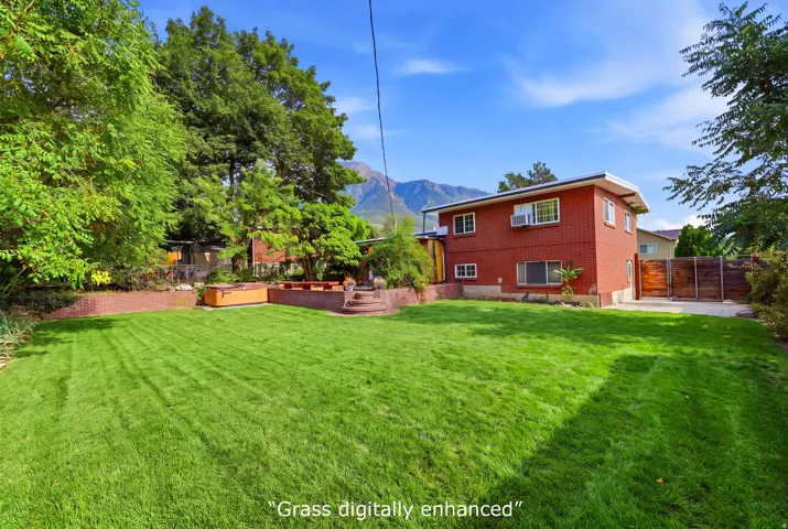Expansive backyard featuring a large lawn, terraced landscaping, and a mountain backdrop