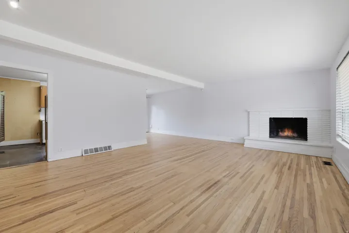 Hardwood flooring, painted brick fireplace with hearth, white window blinds, and white walls