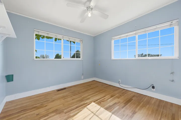 Wood-finish flooring, white window trim, white ceiling fan, built-in shelving, and white baseboards