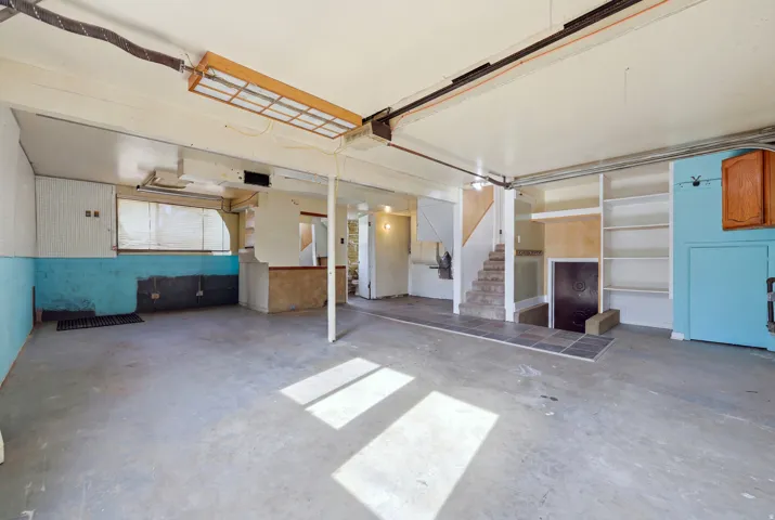Unfinished lower level featuring concrete flooring, built-in shelving, wood-finish cabinetry, and a staircase