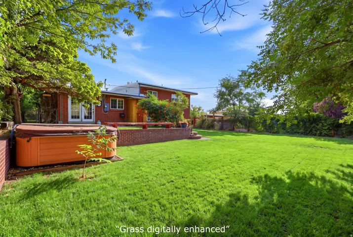 Expansive lawn area with a hot tub, brick retaining wall, mature trees, and a red brick exterior on the home featuring white frame windows