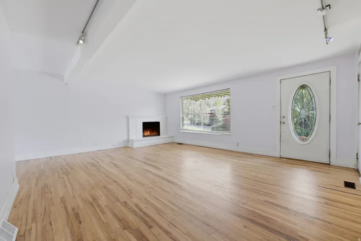 Hardwood flooring, white painted walls, fireplace with tile surround, track lighting, and a front entry door with an oval leaded glass insert