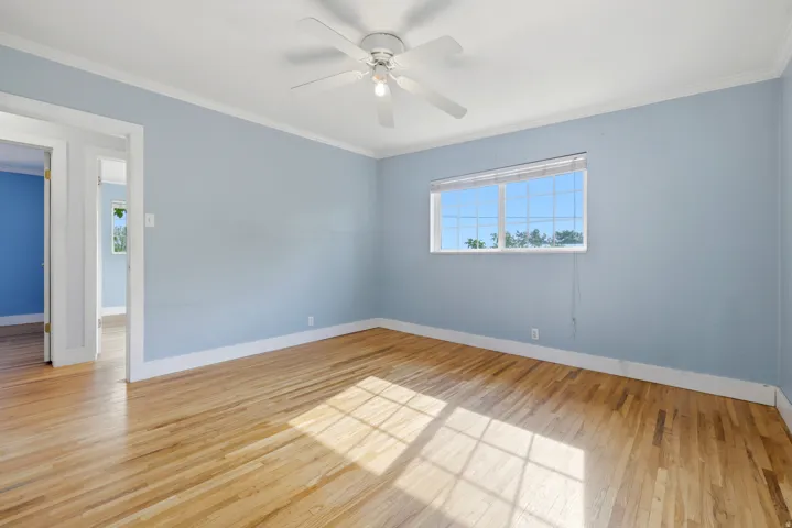 Hardwood flooring, white ceiling fan, single window with blinds, white trim, and light blue walls