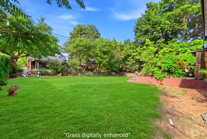 Expansive lawn featuring mature trees and a brick retaining wall