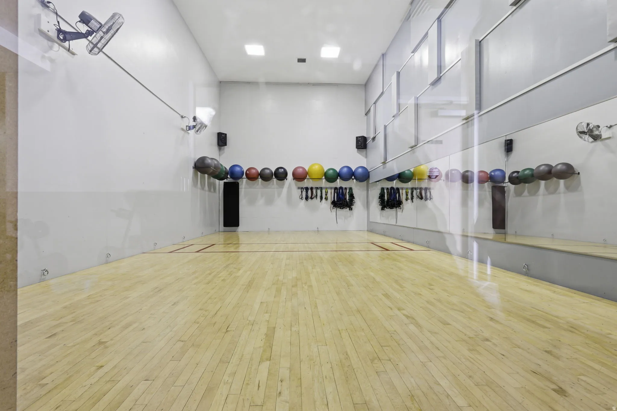 State-of-the-art fitness studio featuring pristine wood-finish flooring, mirrored wall panels, professional recessed and track lighting, and comprehensive equipment storage with medicine balls and resistance gear mounted along the perimeter walls