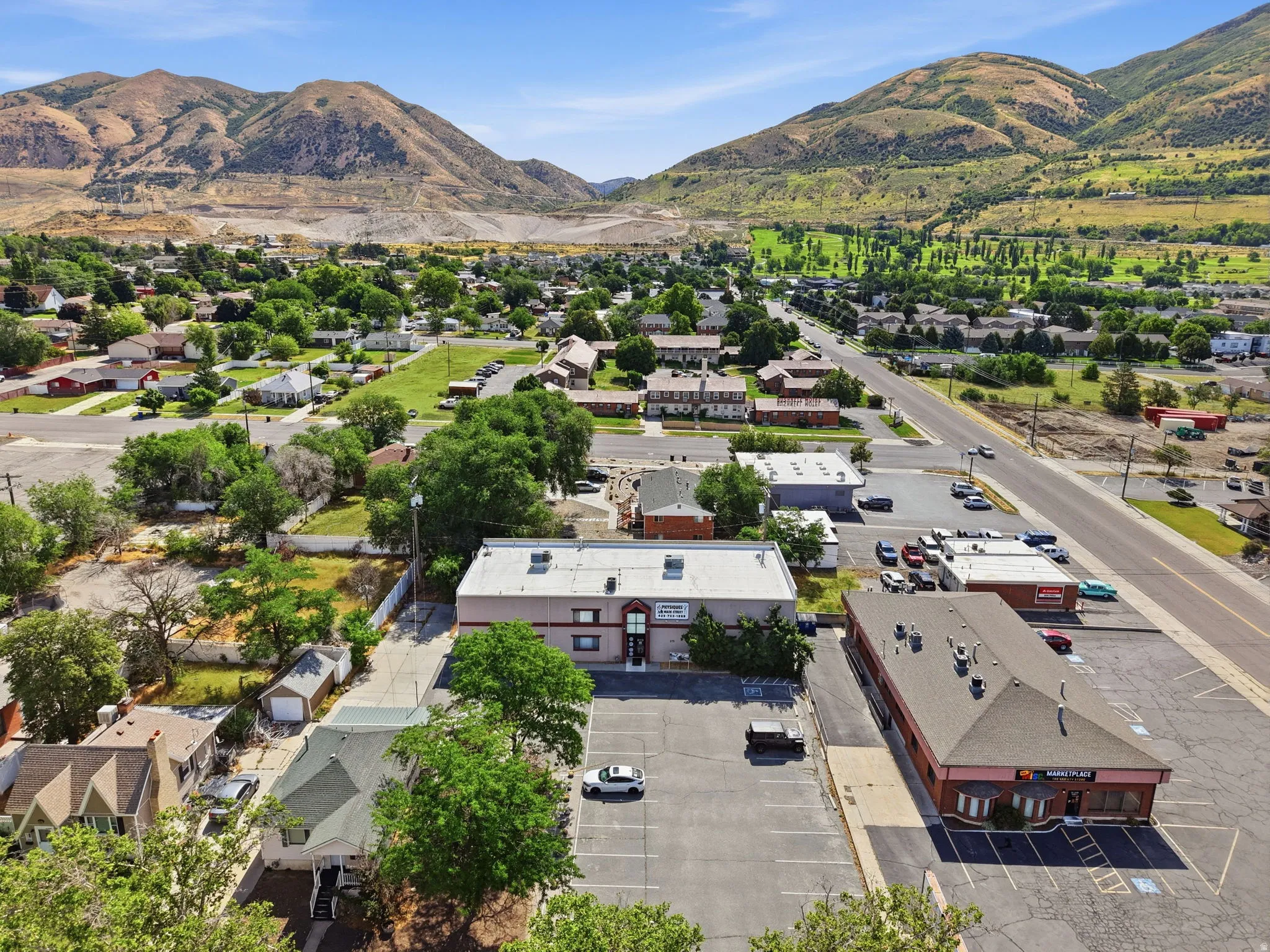 Aerial view showcasing this commercial property positioned along a main thoroughfare, with ample parking facilities and a modern white building structure