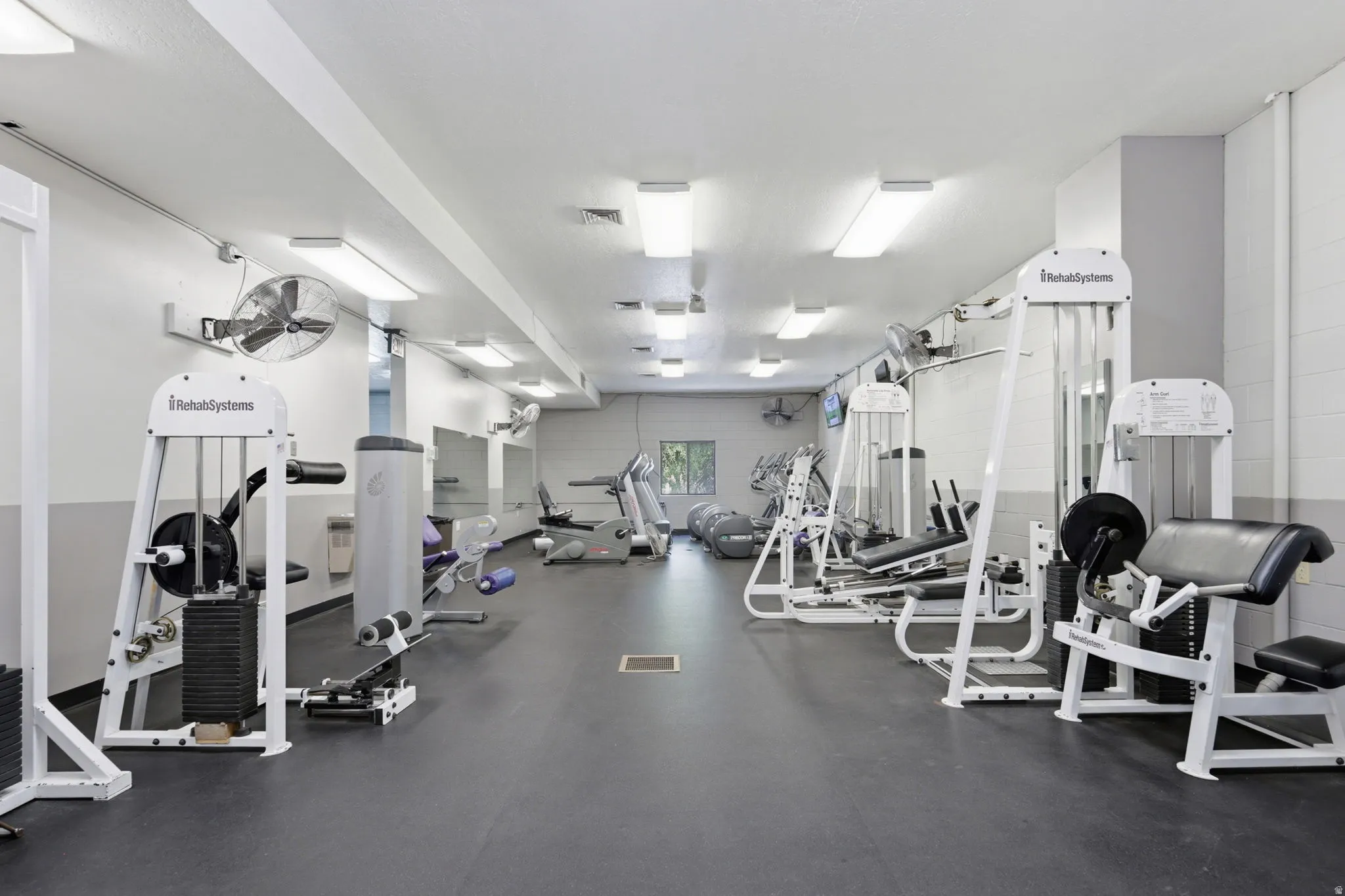 Fitness center featuring multiple weight machines, cardio equipment, and wall-mounted fans
