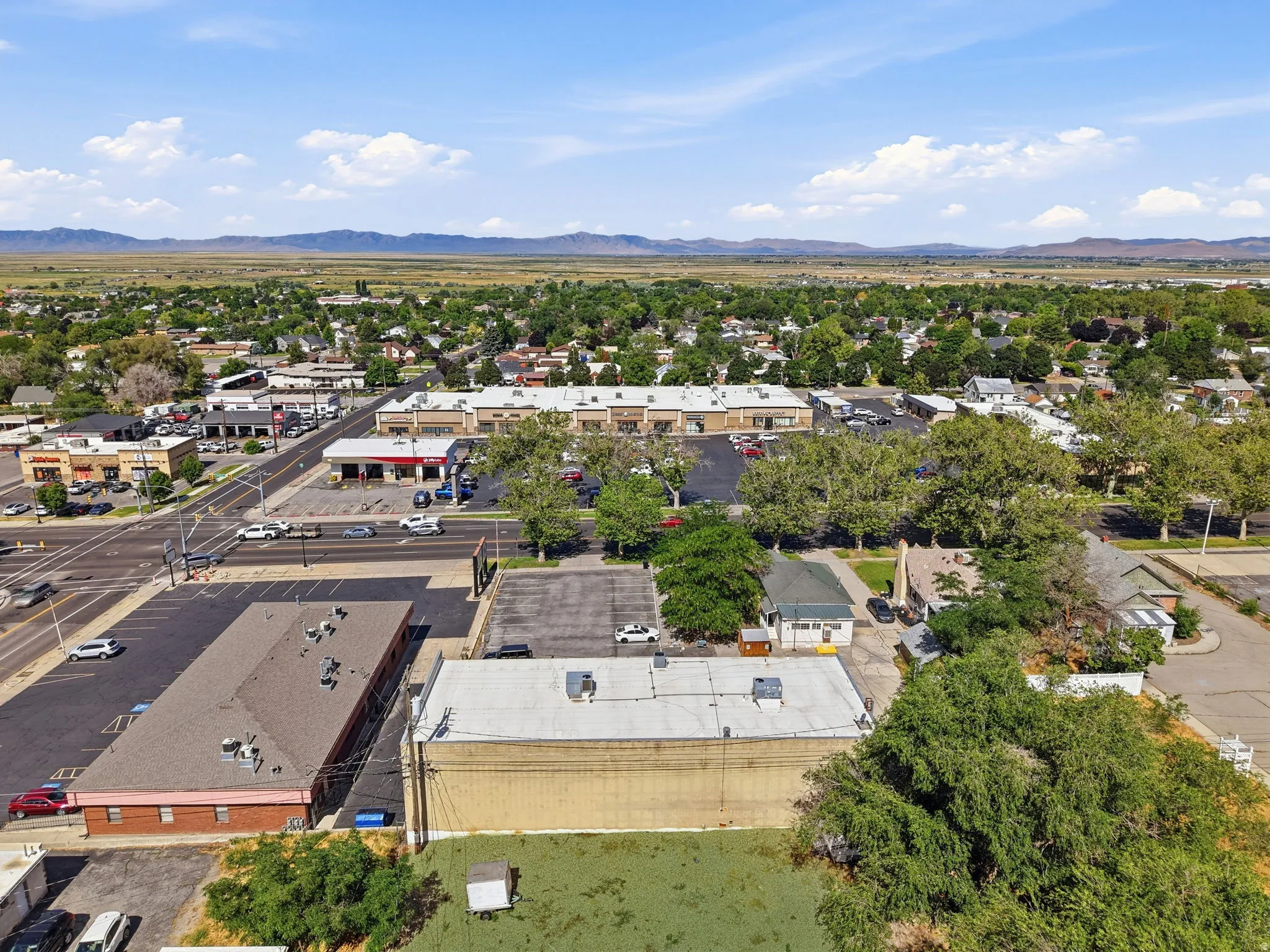 Aerial view showcasing a commercial property with multiple connected buildings featuring flat roofs, expansive asphalt parking areas, and mature landscaping throughout the grounds
