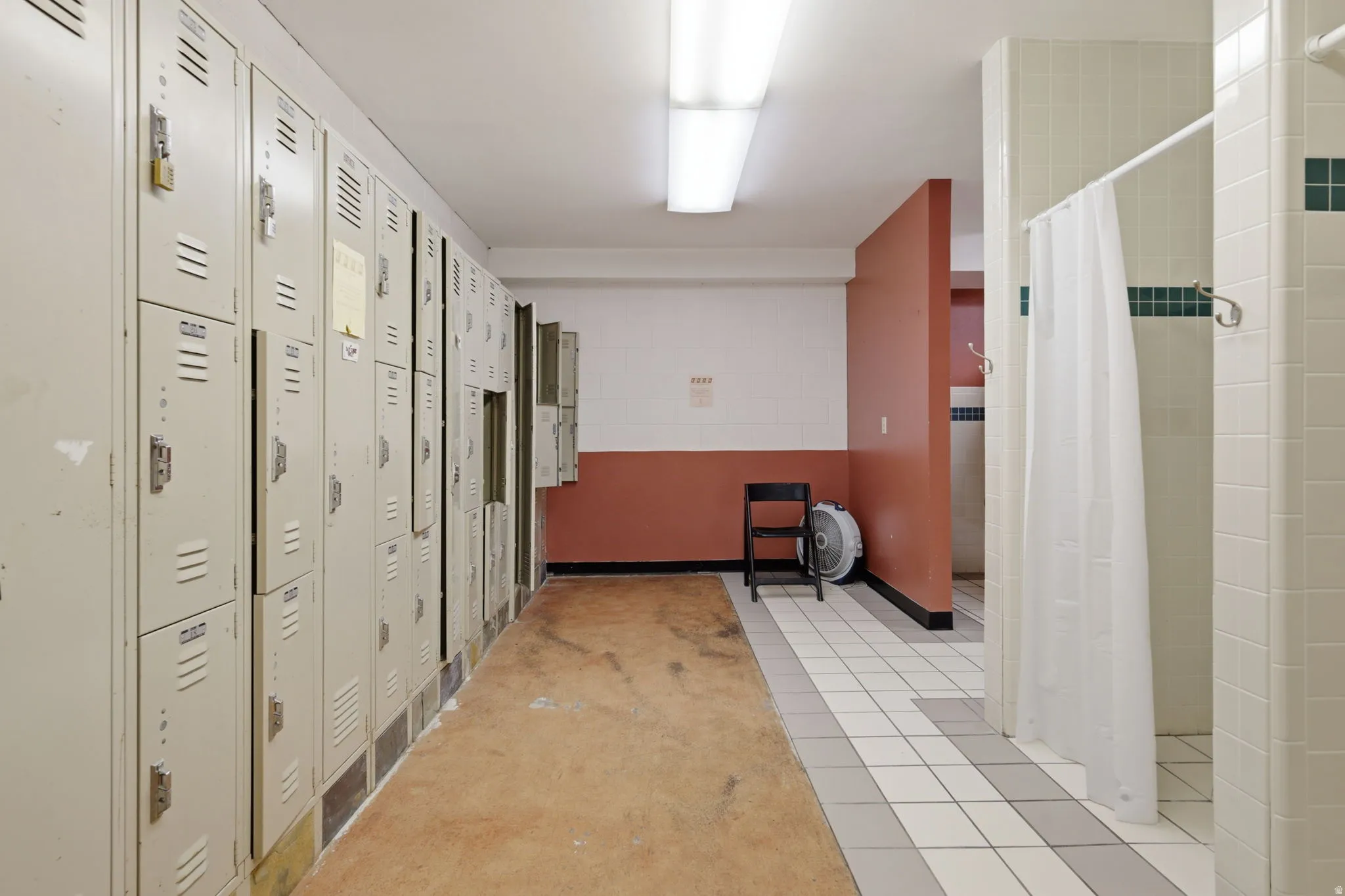 Institutional-style hallway featuring multiple steel locker units with ventilated doors, wood-finish flooring, and ceramic tile accents