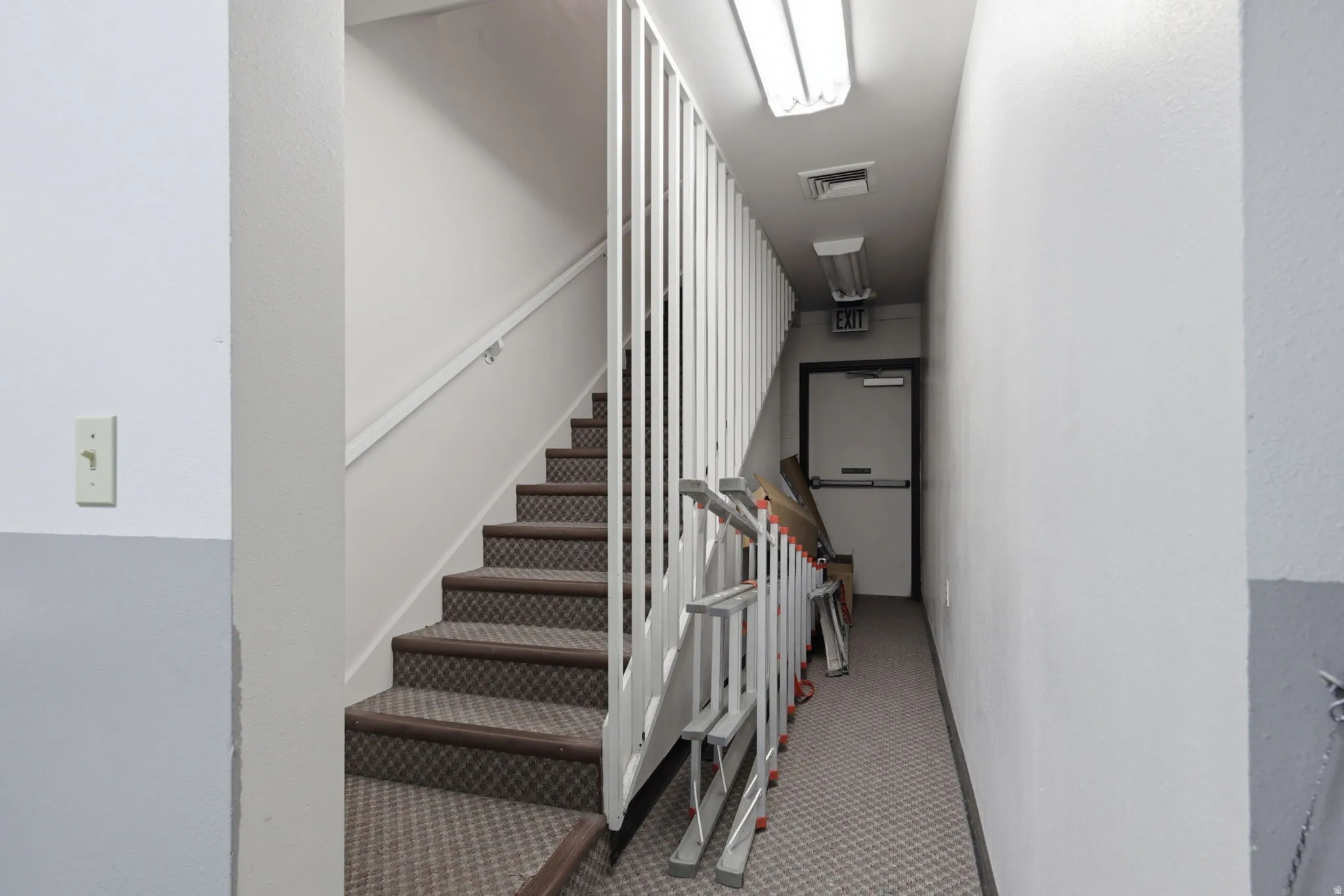 Stairwell with patterned carpeted treads, white wall finishes, and overhead fluorescent lighting
