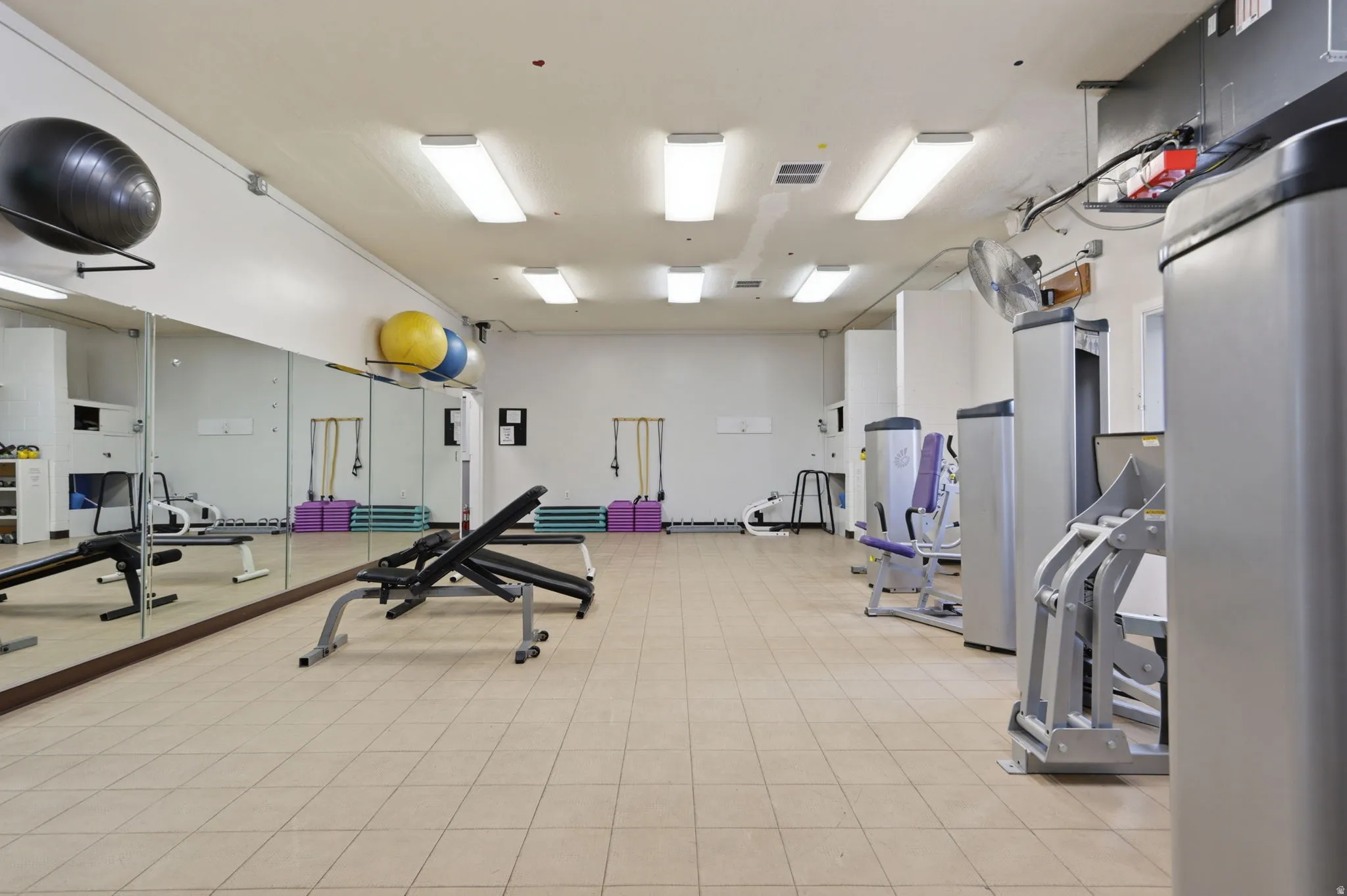 Spacious fitness facility featuring polished tile flooring, mirrored wall panels, recessed and pendant lighting, and a comprehensive selection of cardio and strength training equipment including stationary machines and free weights