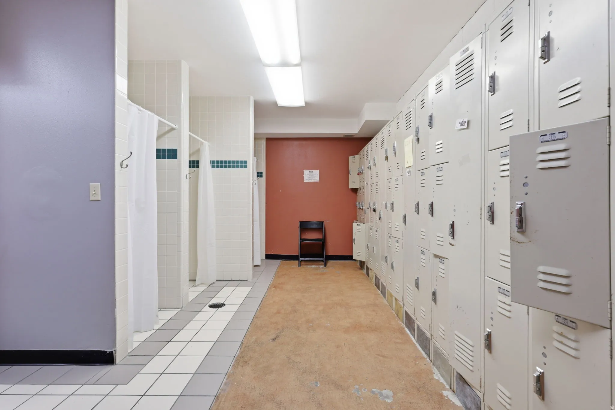 Shower stalls with white tile, a locker wall, and fluorescent ceiling lighting