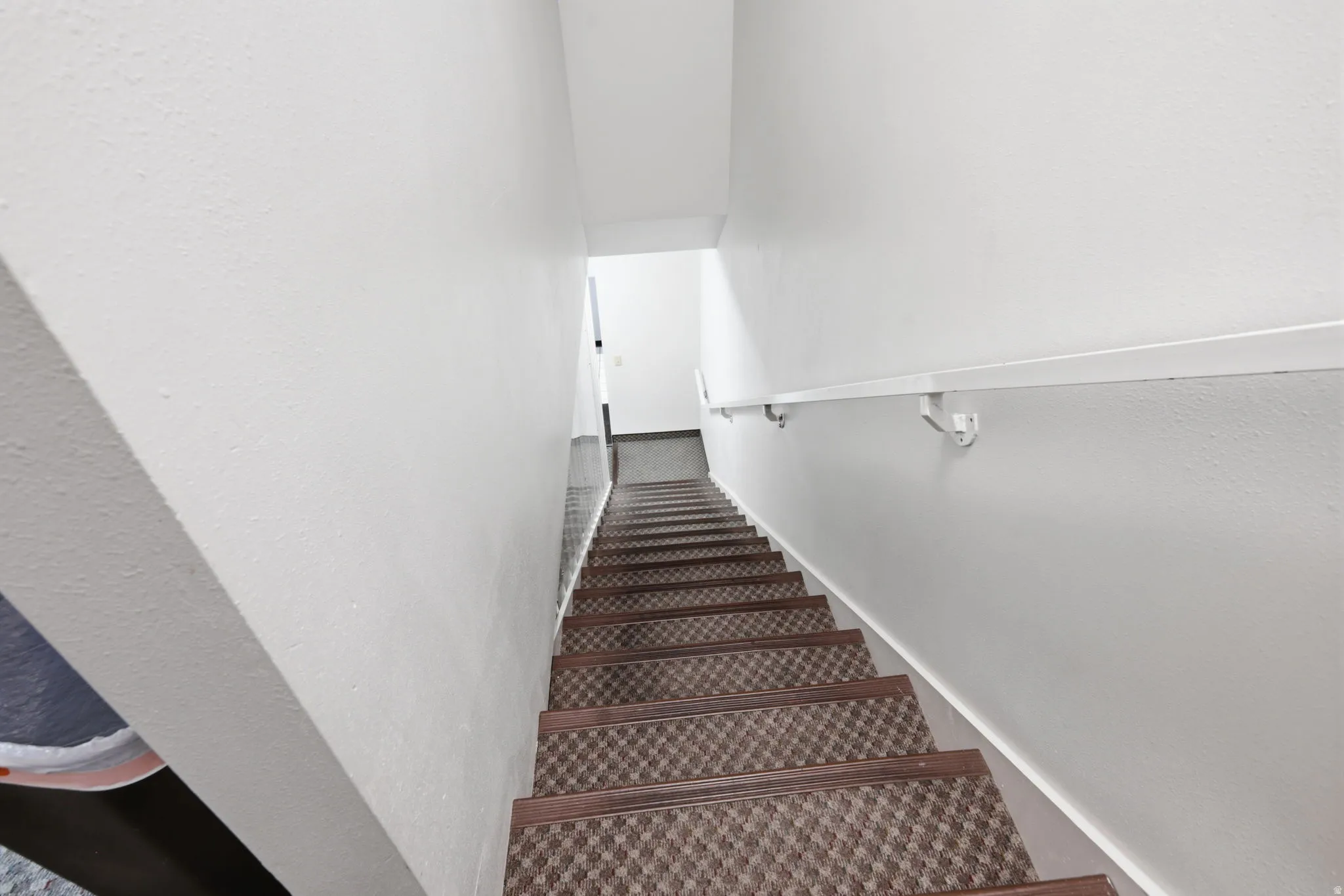 Staircase with patterned carpet runner and brushed metal handrail, leading to bright upper level