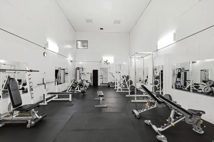Spacious recreation area featuring high ceilings, dark rubber flooring, white walls, and built-in wall mirrors