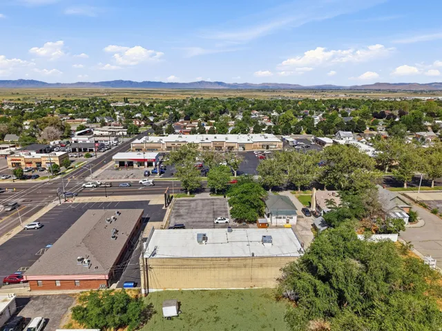 Aerial view showcasing a commercial property with multiple connected buildings featuring flat roofs, expansive asphalt parking areas, and mature landscaping throughout the grounds
