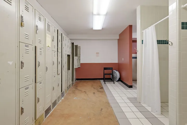Institutional-style hallway featuring multiple steel locker units with ventilated doors, wood-finish flooring, and ceramic tile accents