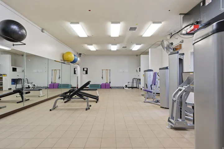 Spacious fitness facility featuring polished tile flooring, mirrored wall panels, recessed and pendant lighting, and a comprehensive selection of cardio and strength training equipment including stationary machines and free weights