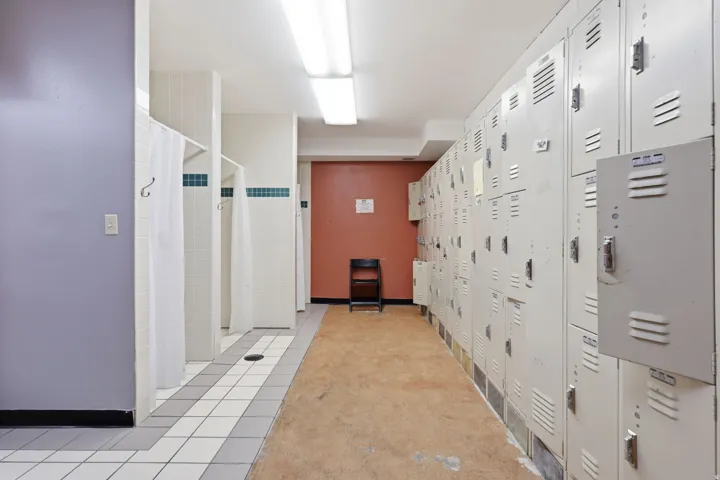Shower stalls with white tile, a locker wall, and fluorescent ceiling lighting