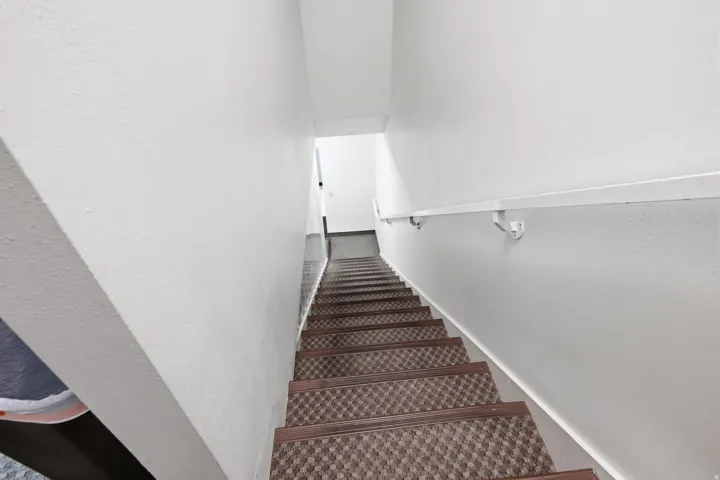 Staircase with patterned carpet runner and brushed metal handrail, leading to bright upper level