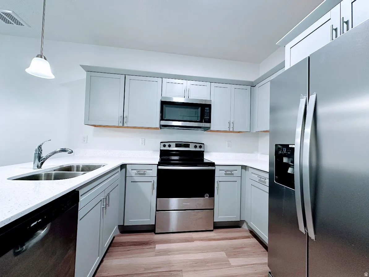 Kitchen featuring light gray cabinetry, white countertops, stainless steel appliances, and wood-finish flooring
