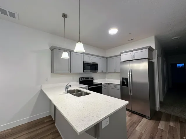 Modern kitchen featuring grey cabinetry, stainless steel appliances, quartz countertops, and wood-finish flooring