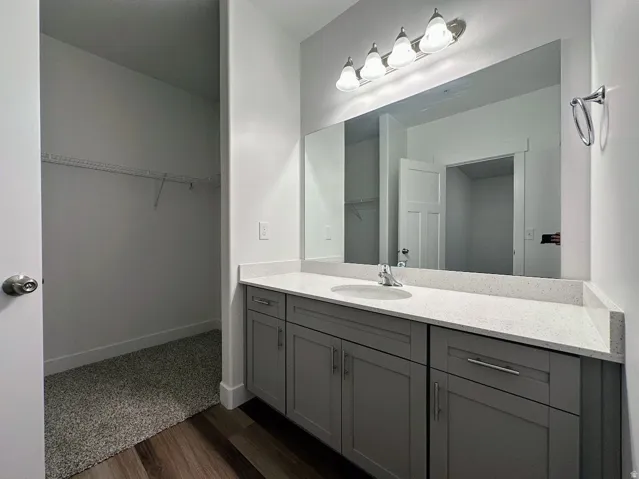 Bathroom vanity with a white countertop and integrated sink, under-cabinet storage, and wood-finish flooring