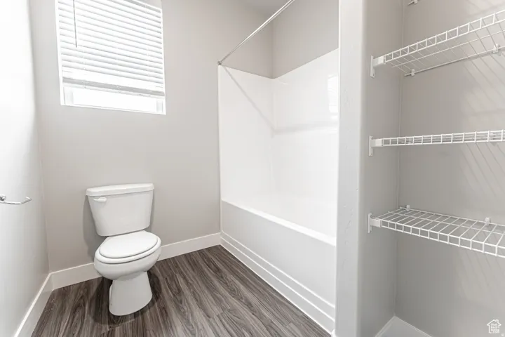White shower-tub combination, wood-finish flooring, white toilet, and built-in wire shelving