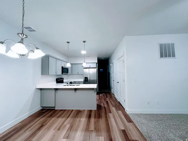 Open-concept living space with wood-finish flooring, light gray cabinetry, and stainless steel appliances