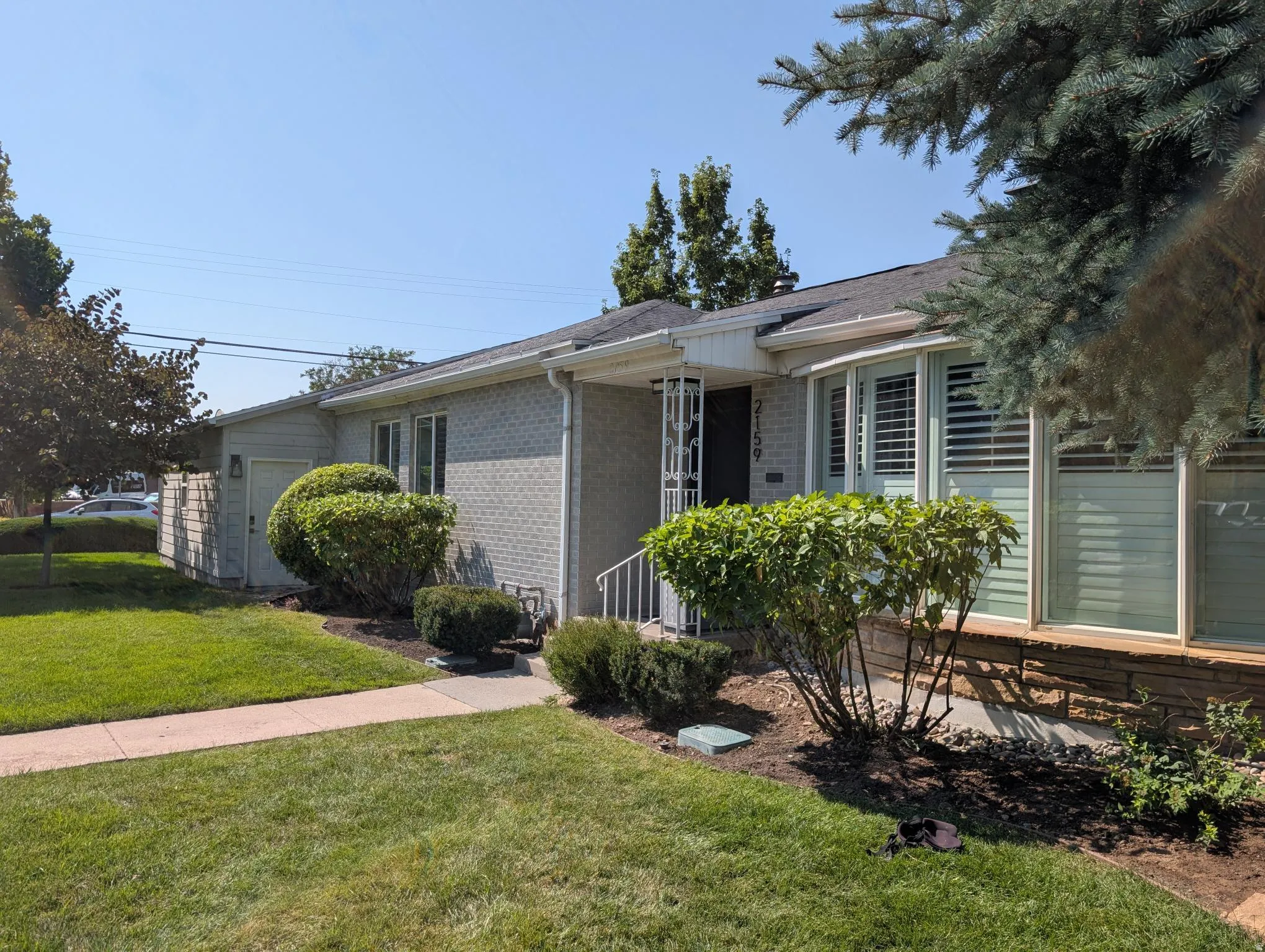 Charming single-story brick residence featuring a welcoming front entry with shuttered windows, manicured foundation landscaping including shaped hedges, and mature evergreen trees