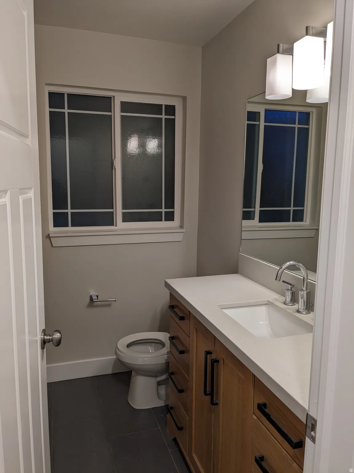 Wood-finish vanity with black hardware, white rectangular sink, and light-toned countertop