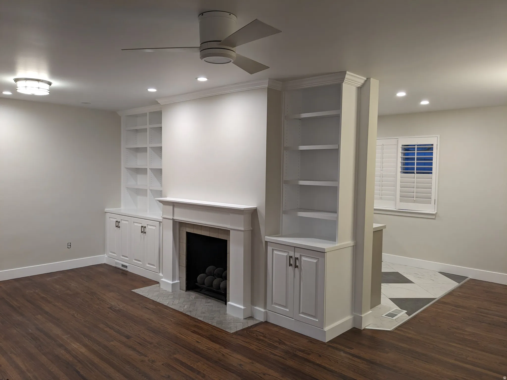 Built-in shelving, fireplace with hearth, wood-finish flooring, recessed lighting, and window with plantation shutters