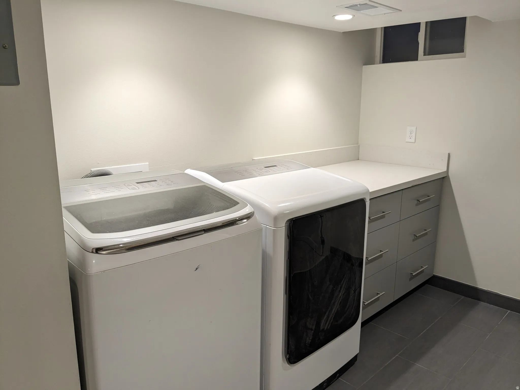 Laundry area featuring gray cabinetry with brushed nickel hardware, light-toned countertop, and dark-toned floor tiling
