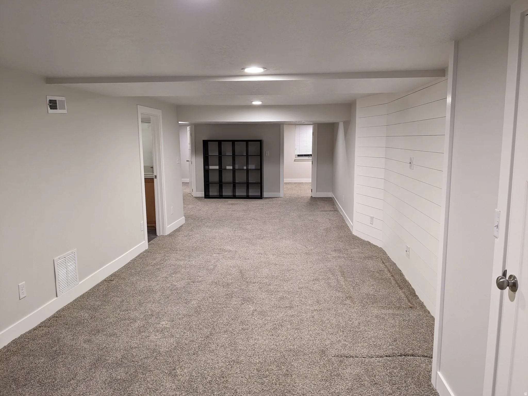 Recessed lighting, light gray carpeting, white painted walls, white shiplap accent wall, and white trim throughout