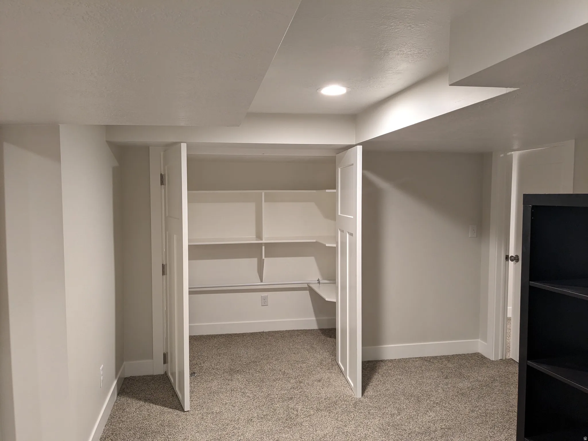 Finished basement space featuring built-in shelving with adjustable shelves, recessed lighting, and neutral wall finishes