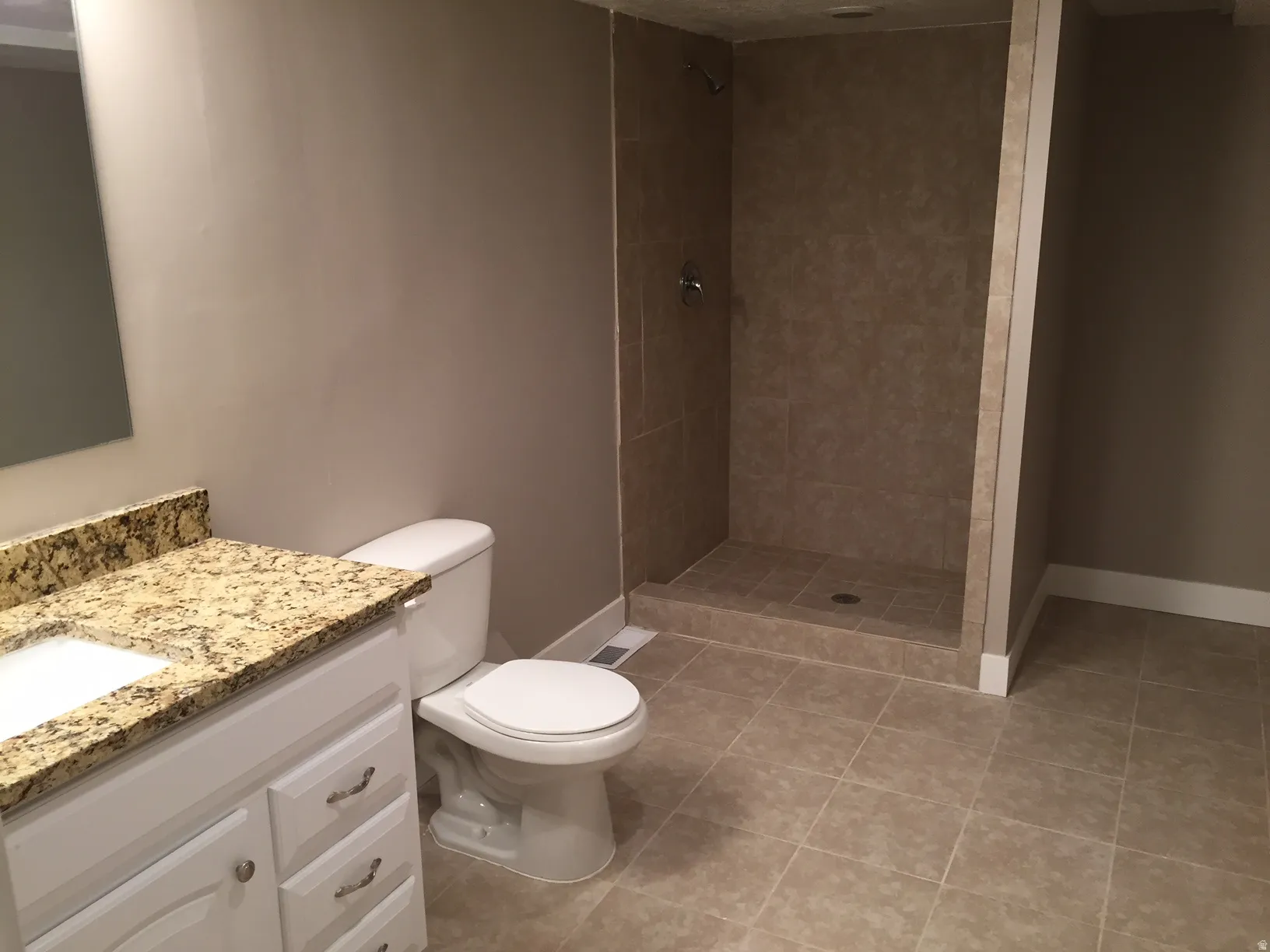 White vanity with a stone countertop, an undermount sink, and a tiled shower