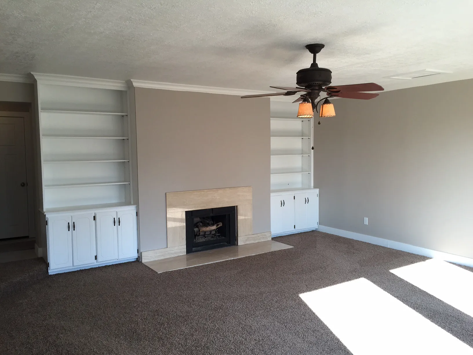 Built-in shelving with lower cabinetry, central fireplace with stone surround, and ceiling fan with integrated lighting