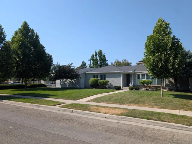 Charming single-story residence with a manicured front lawn, mature landscaping, and established shade trees